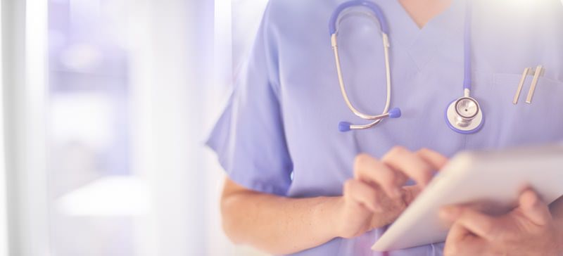 Female surgeon wearing scrubs, looking at her patients records on her digital tablet