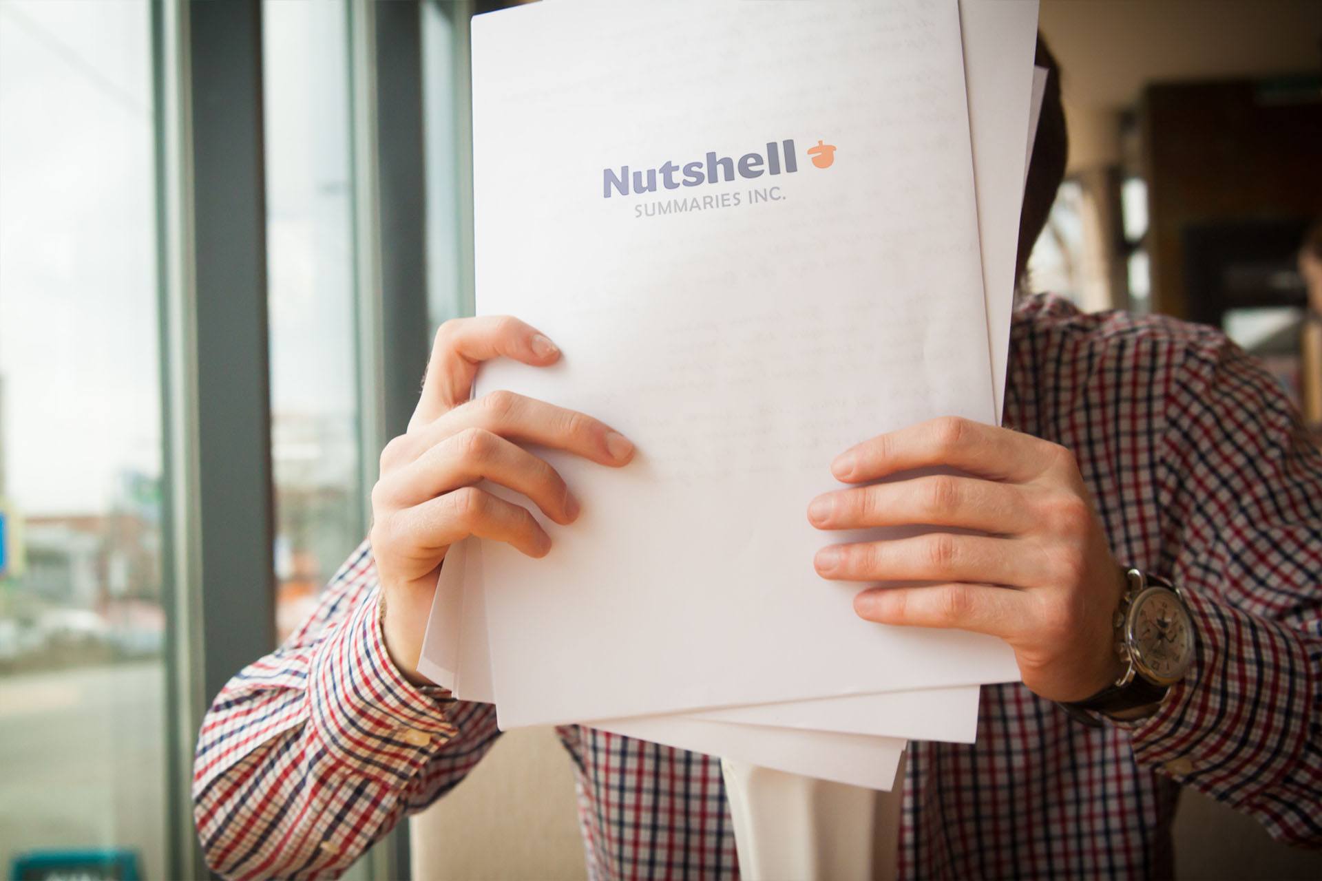 young office worker holding paperwork up to forehead with nutshell summaries logo on rear of paperwork