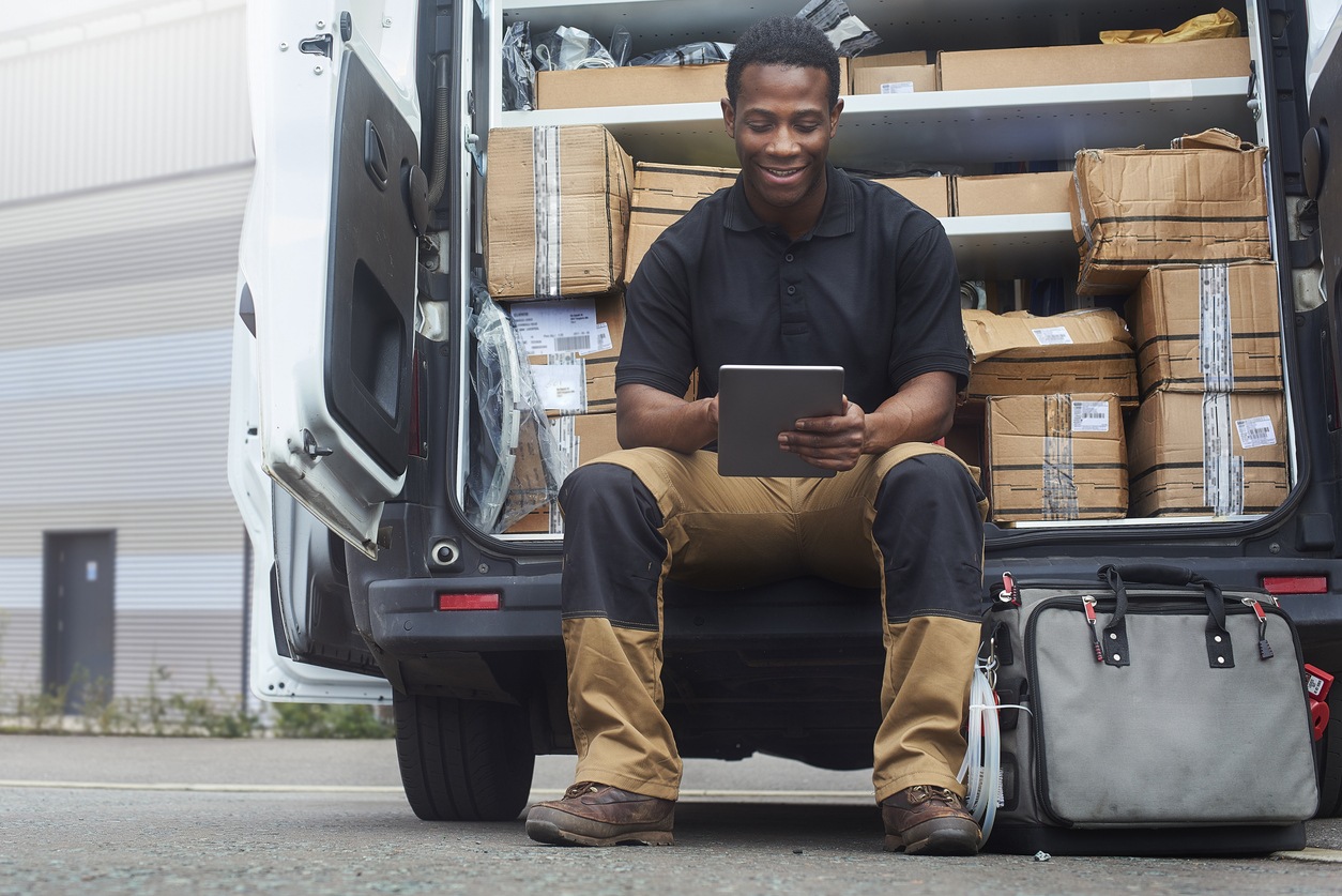 Service engineer sat in the back of his van interacting with job management tablet