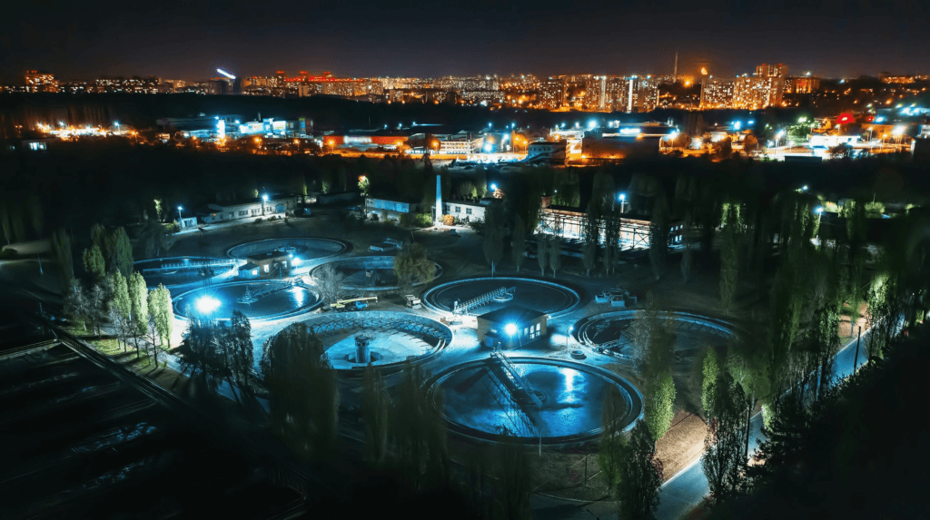 An illuminated water treatment facility with a city skyline in the background